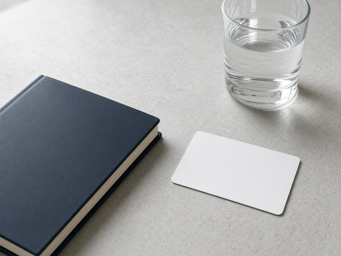 A blank card beside a closed notebook and a glass of water